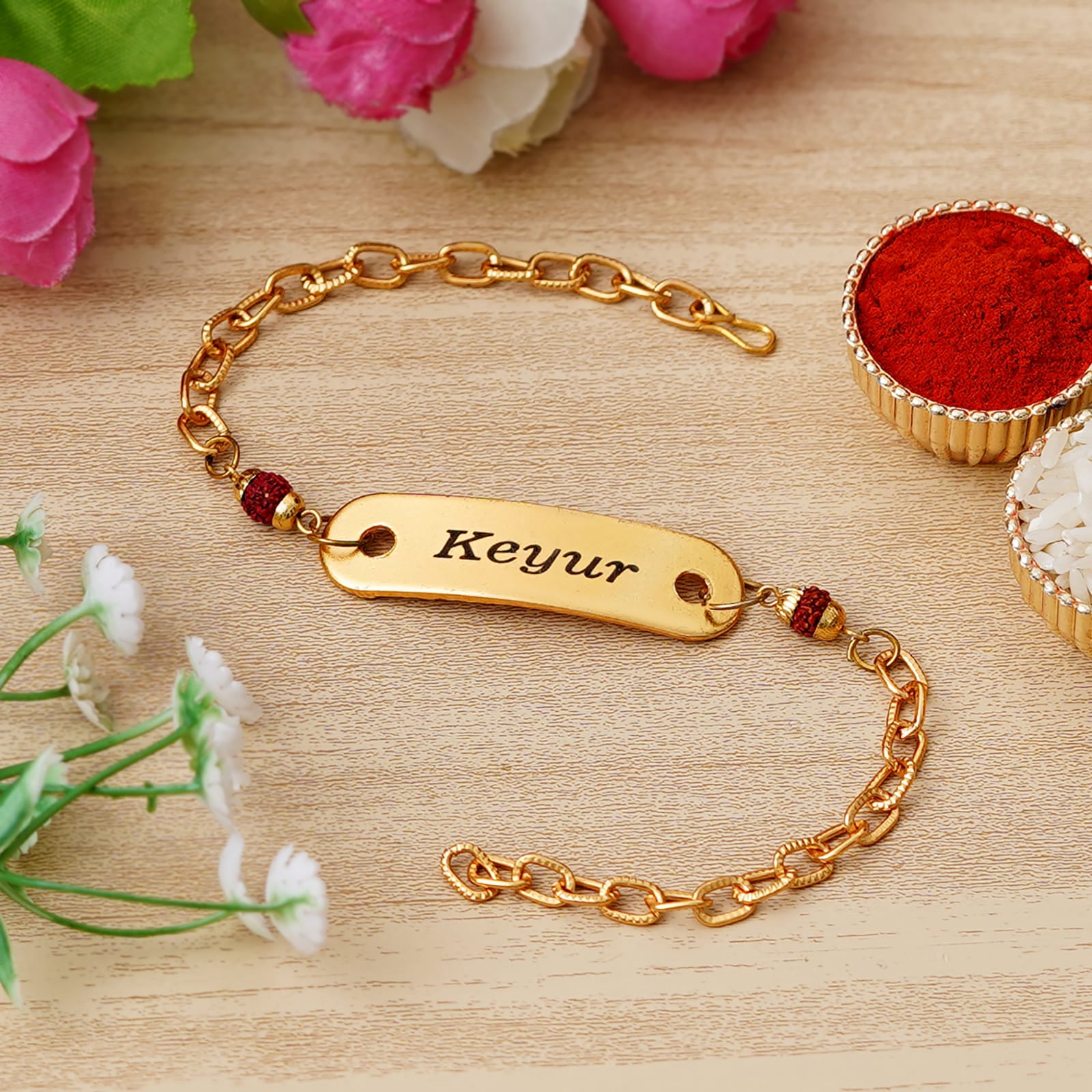 Gold bracelet with engraved name 'Keyur' on a wooden surface with flowers and red powder - The Gifting Era
