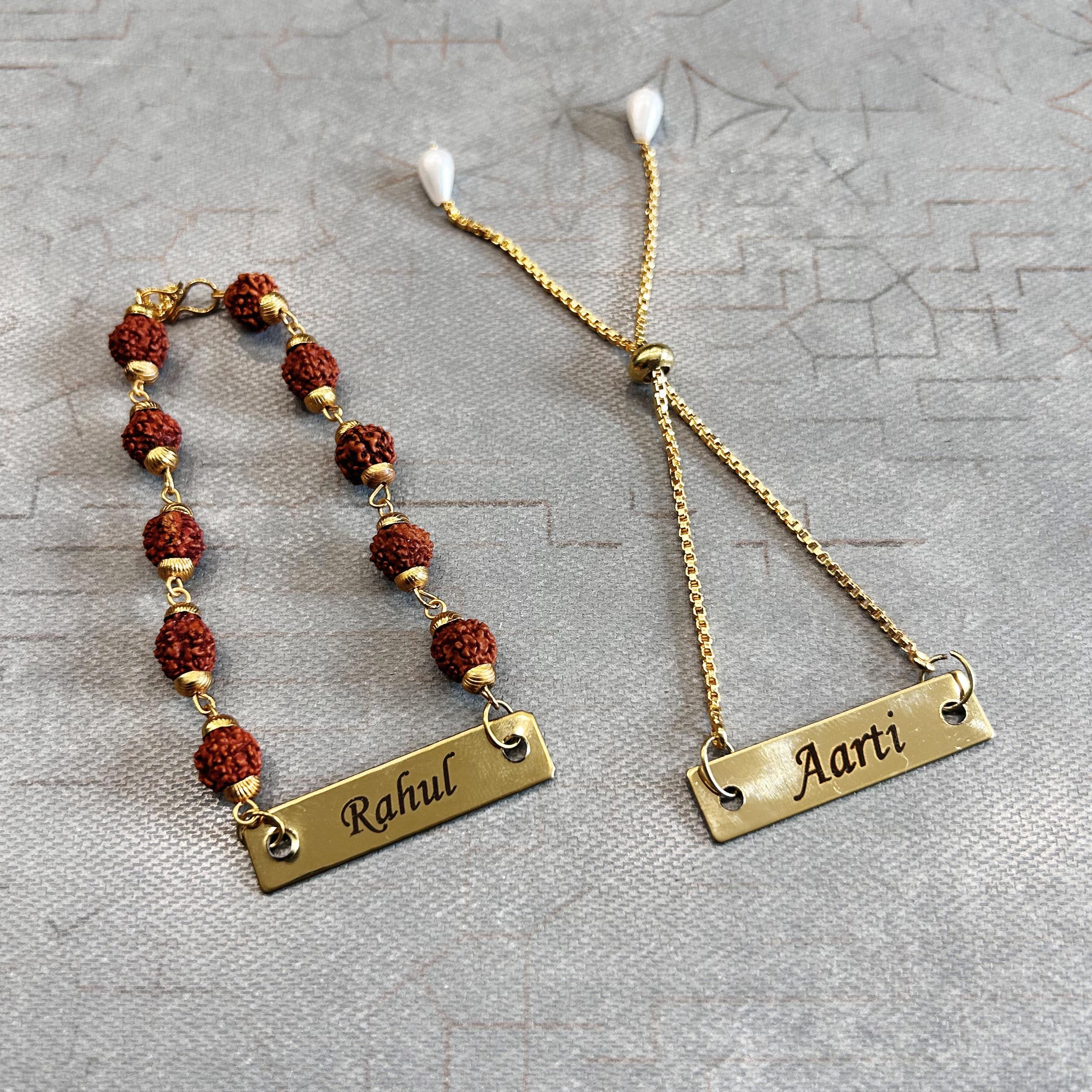 Two name bracelets, one with red beads and the other gold chain, on a textured gray surface. - The Gifting Era