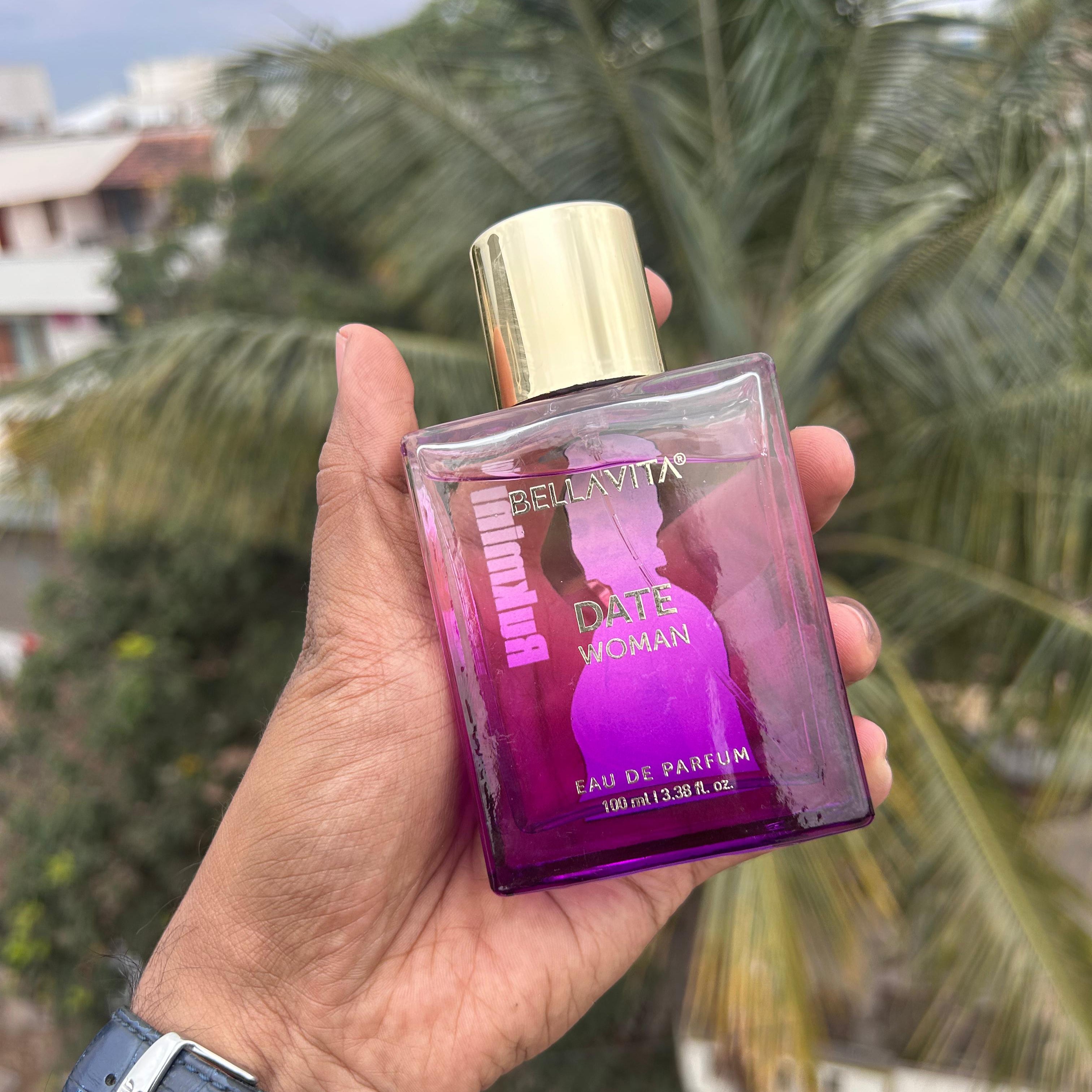 Hand holding a purple perfume bottle with a gold cap against a blurred outdoor background - The Gifting Era