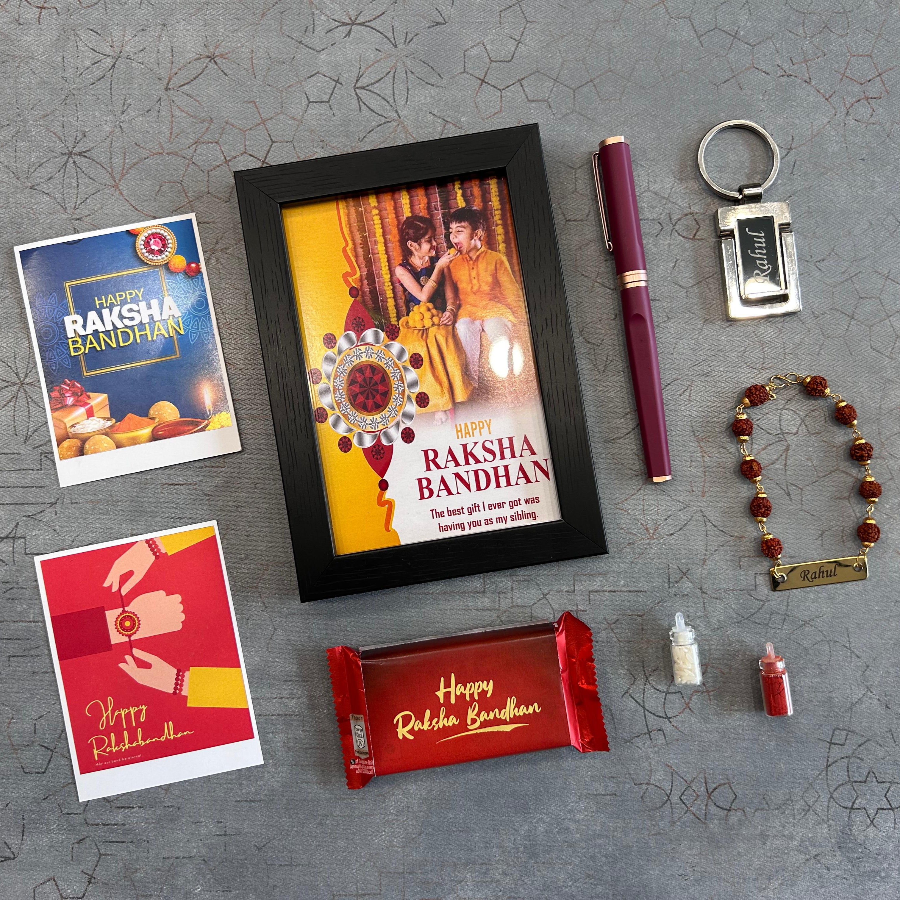 Raksha Bandhan-themed items including a photo frame, cards, pen, keychain, bracelet, and candy on a gray surface. - The Gifting Era