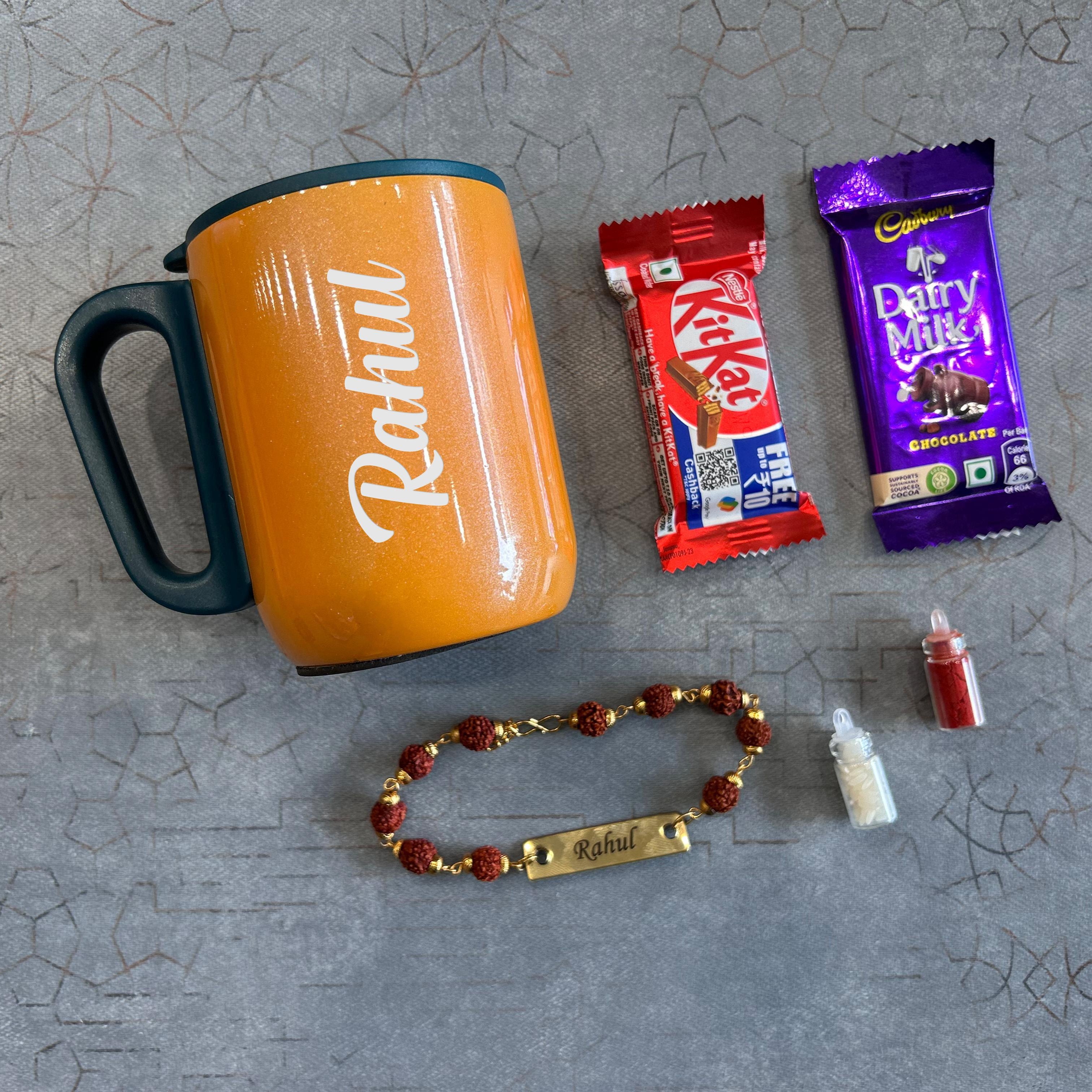 Orange mug with 'Rahul' branding, KitKat bar, Dairy Milk chocolate, beaded bracelet, and small bottle on a textured gray surface. - The Gifting Era
