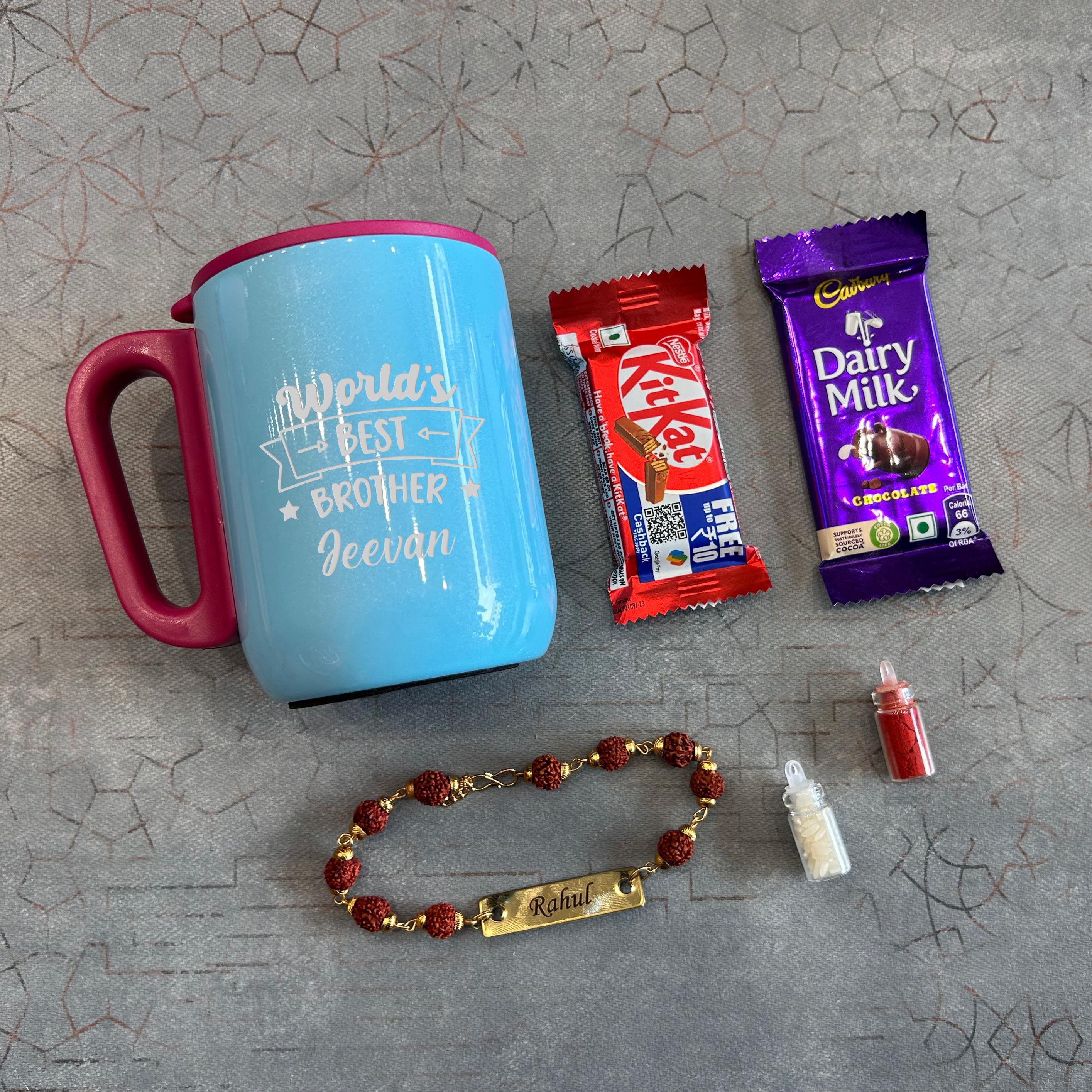 Blue mug with pink handle, KitKat bar, Dairy Milk bar, beaded bracelet, and small bottle on a textured surface - The Gifting Era