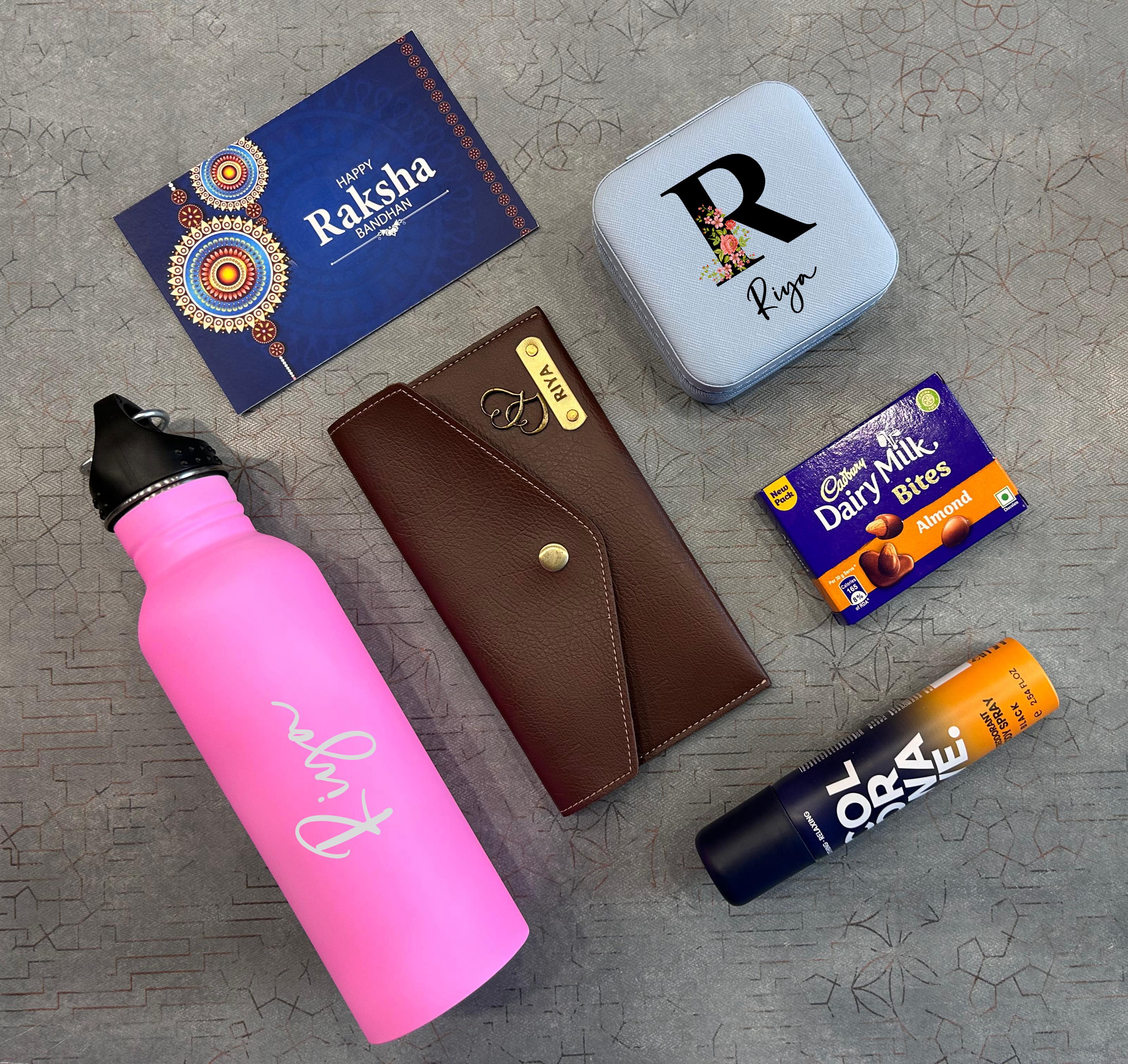 Collection of Raksha Bandhan-themed items including a pink water bottle, brown wallet, blue card, and chocolate bars on a textured surface. - The Gifting Era