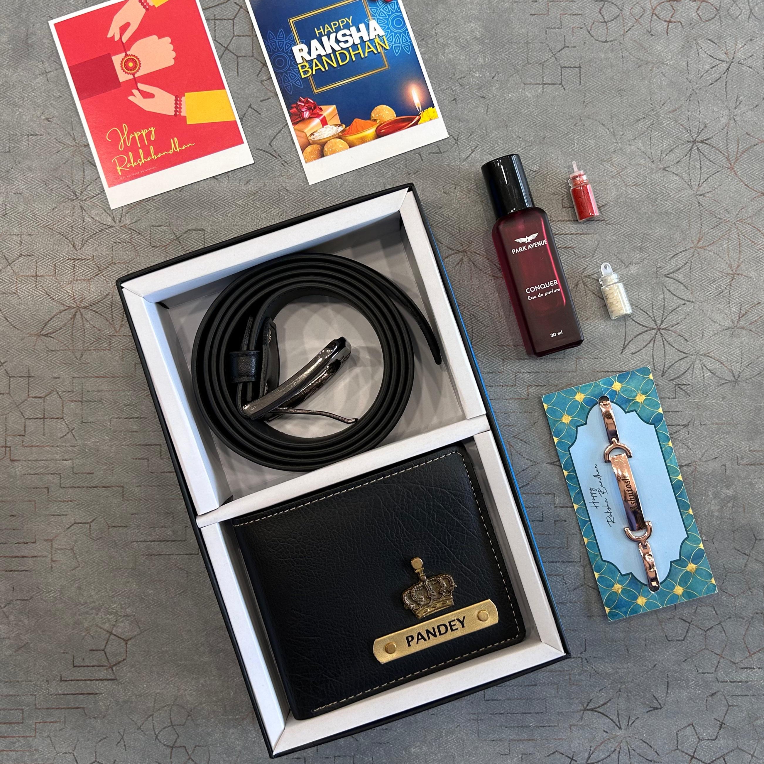 Black wallet with 'PANDEY' engraving, cable, and small bottles on a textured surface with 'Happy Raksha Bandhan' cards. - The Gifting Era