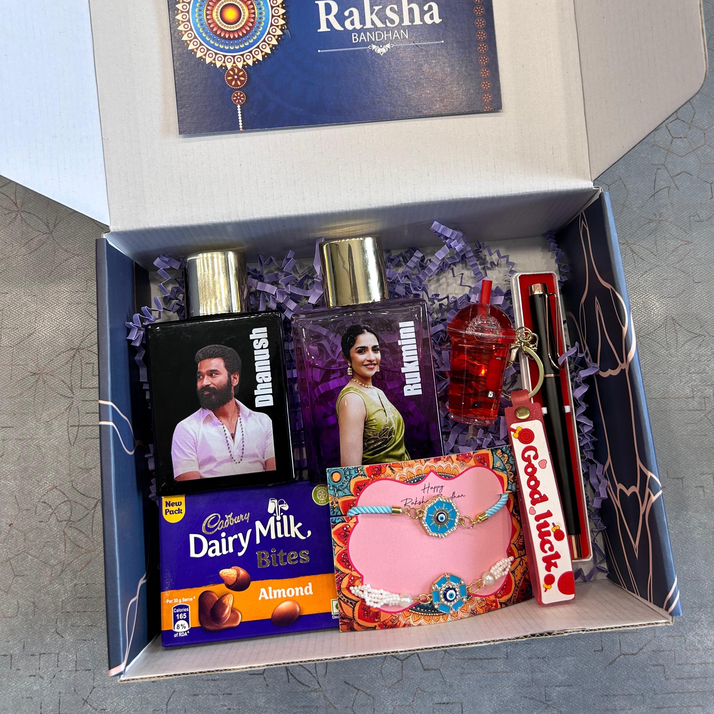 Gift box with Raksha Bandhan-themed items including a card, photo frames, and a bottle on a gray surface. - The Gifting Era