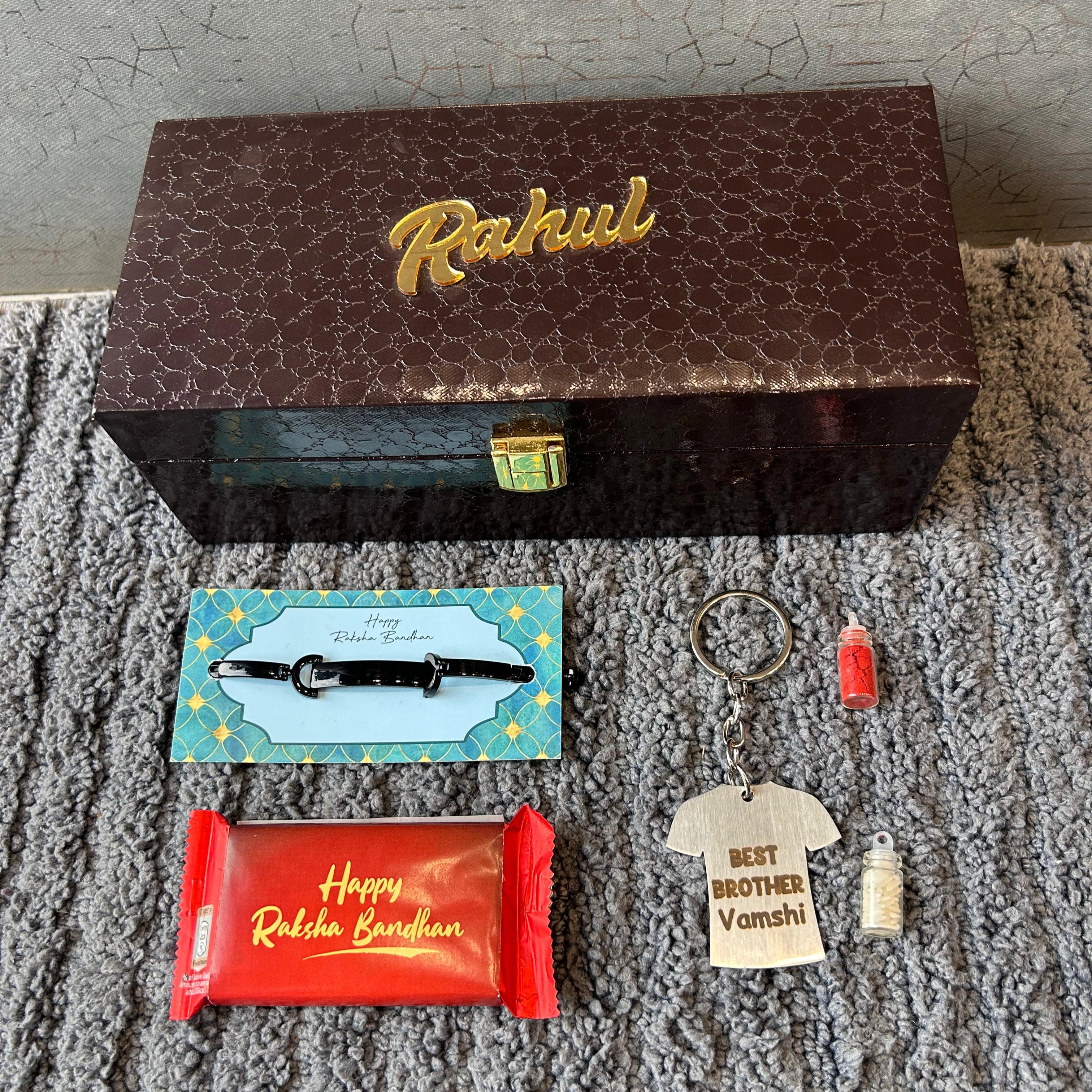 Collection of small items including a chocolate, keychain, and decorative pieces on a textured surface with a box labeled 'Rahul'. - The Gifting Era