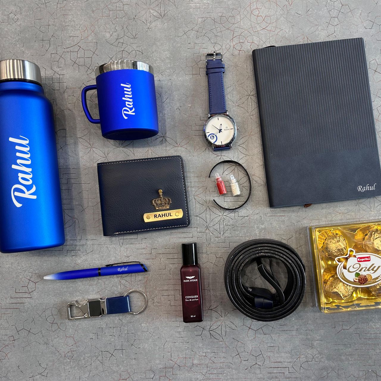 Collection of personalized items including a water bottle, mug, wallet, and accessories on a gray surface.  - The Gifting Era