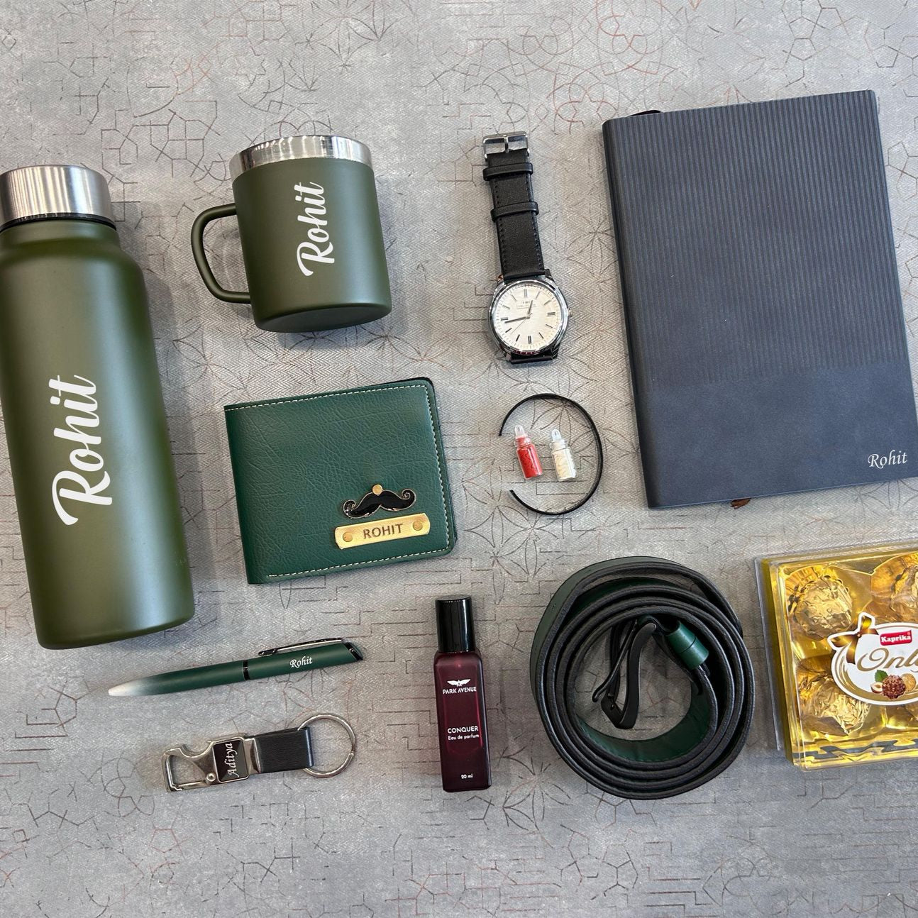 Collection of branded items including a water bottle, mug, wallet, watch, notebook, and others on a textured surface.  - The Gifting Era