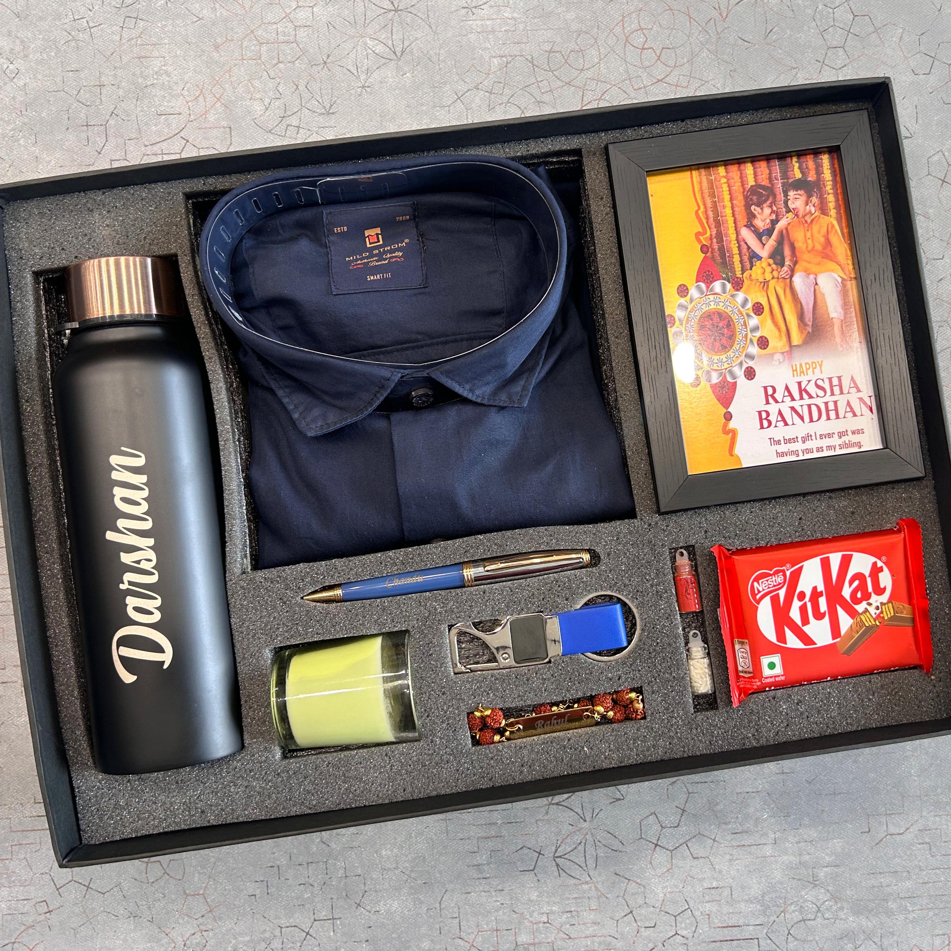 Gift set with Darshwin water bottle, navy shirt, Raksha Bandhan card, KitKat bar, and other items in a box. - The Gifting Era
