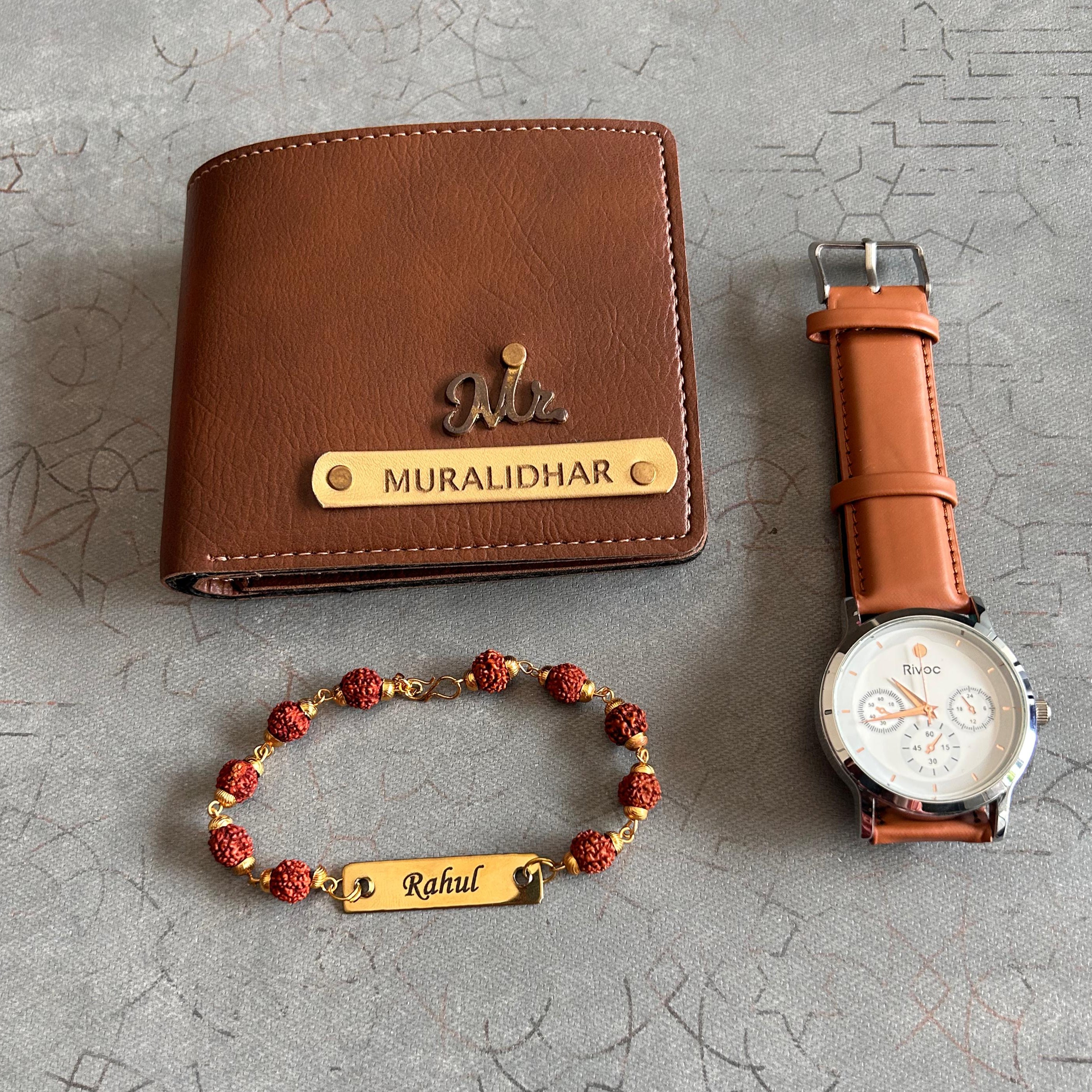 Brown leather wallet, watch, and bracelet with engraved names on a textured gray surface