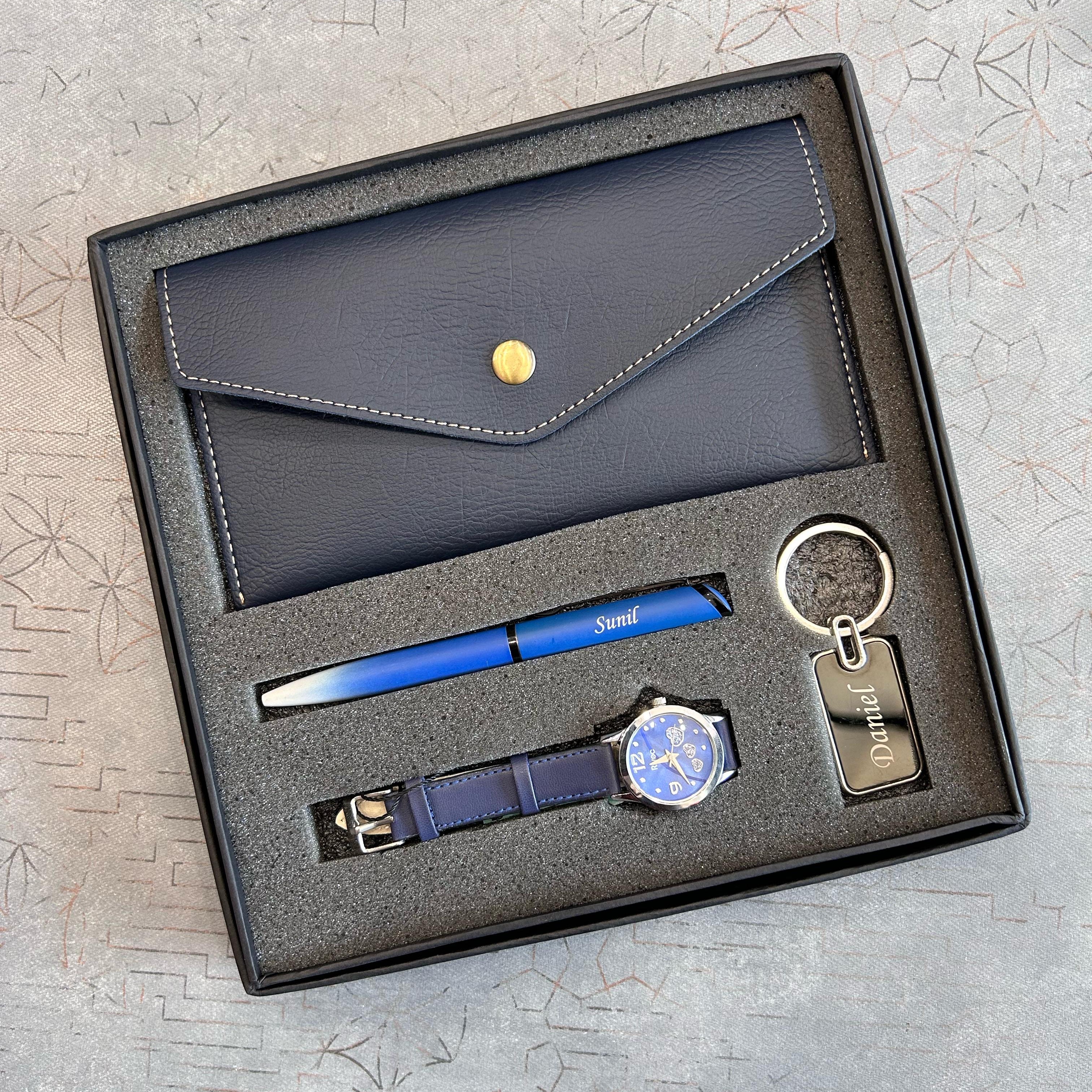 Set of stationery items including a pen, keychain, watch, and wallet in a box on a textured surface.